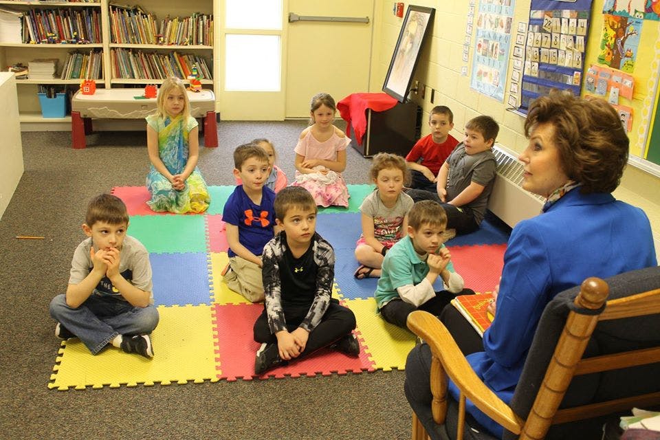 Adult reading to a group of children sitting on a colorful mat