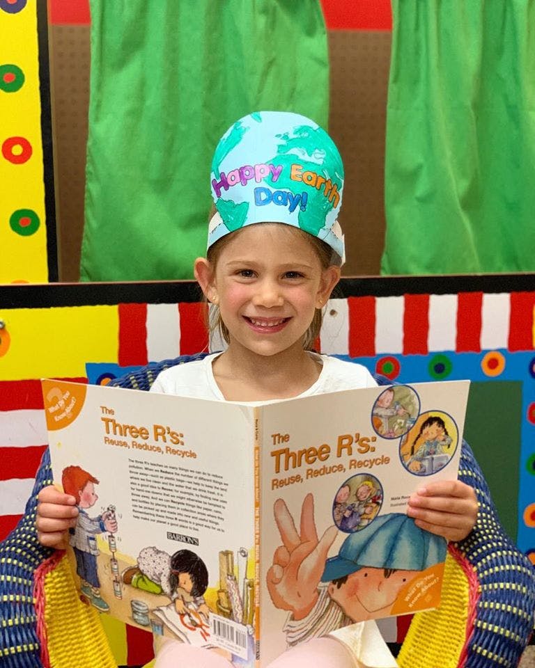 Child wearing a "Happy Earth Day!" hat and reading a book