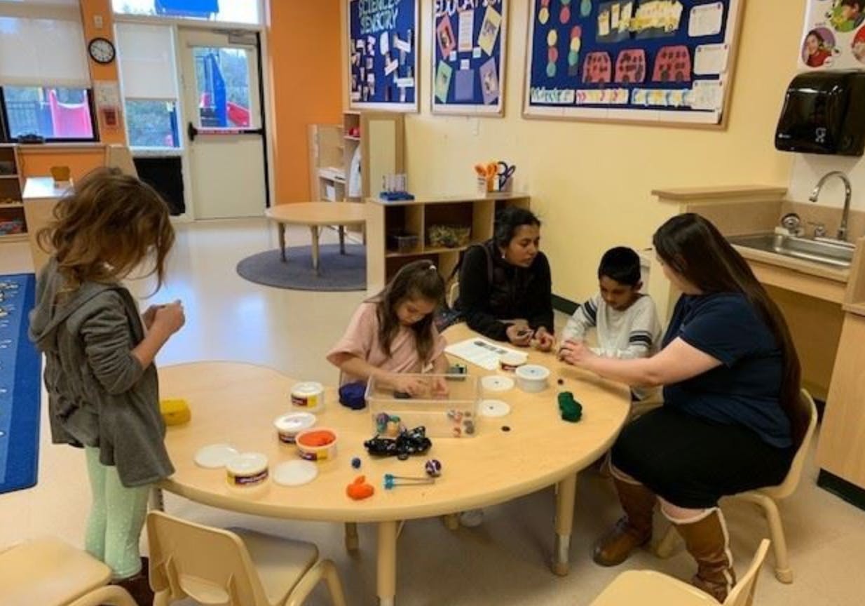 Adults and children at a table with craft supplies in a classroom