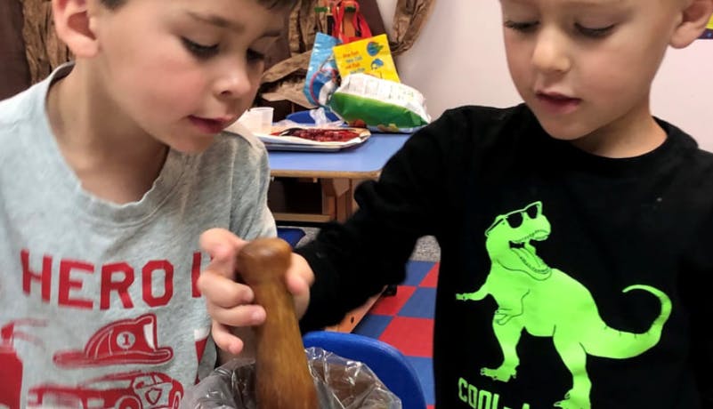 Two children using a wooden pestle in a classroom