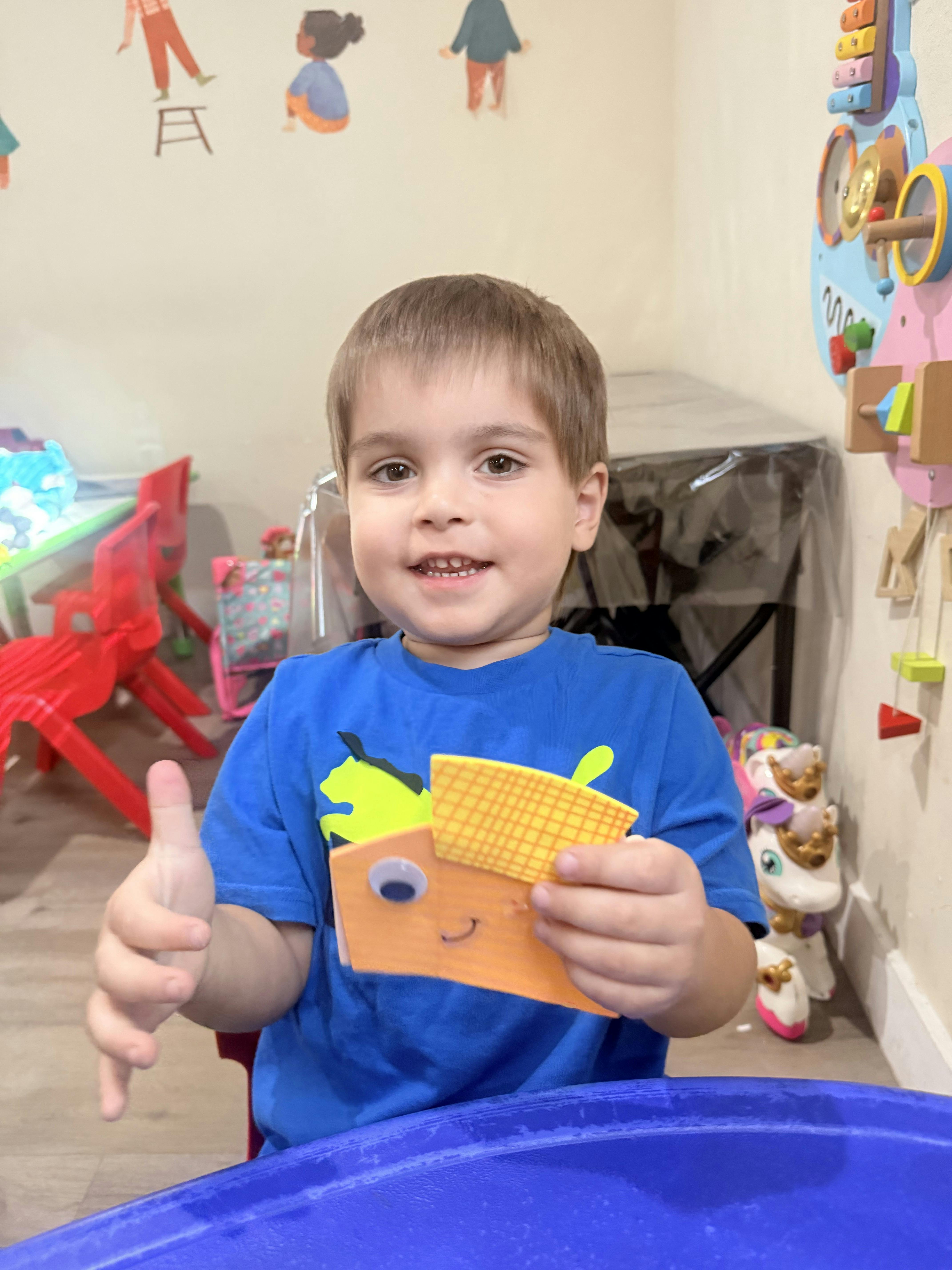 Child holding a small crafted paper object in a classroom