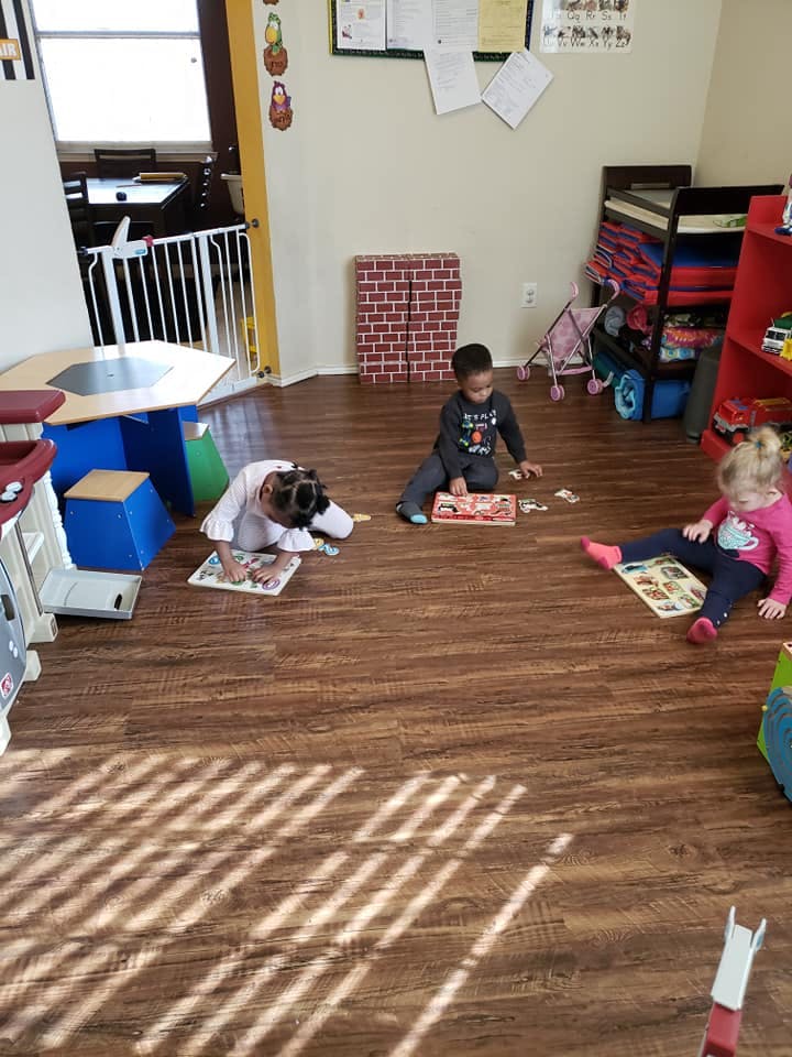 Three children playing with puzzles on a wooden floor in a room