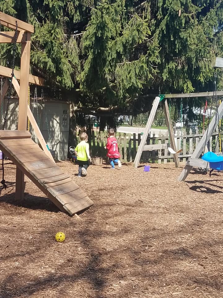 Two children playing on a playground with a slide and swings