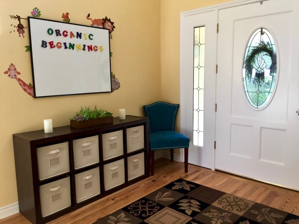 Entryway with a storage unit, blue chair, and white board with "ORGANIC BEGINNINGS"