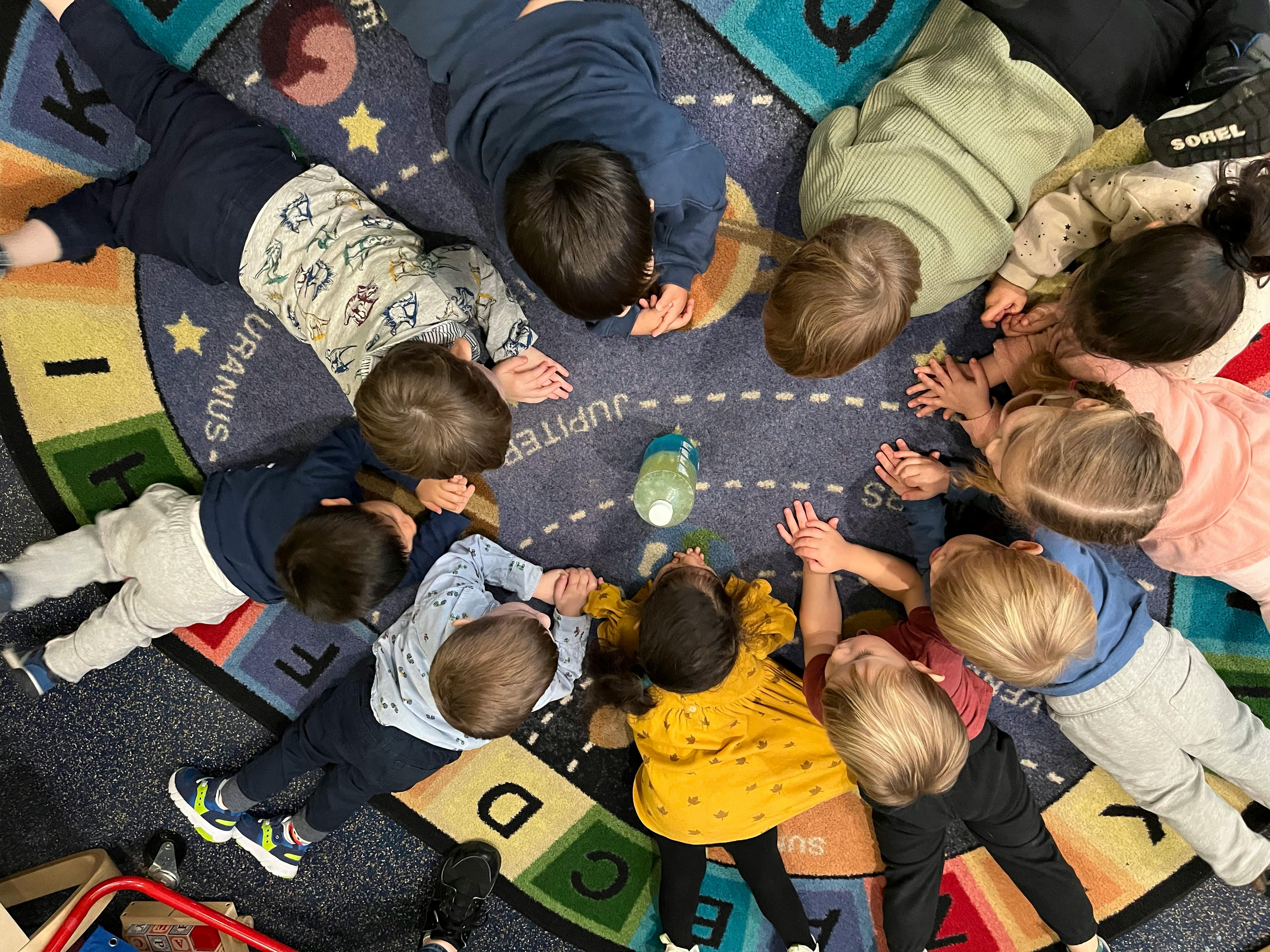 Children lying in a circle on a rug, rug looking at something in the center