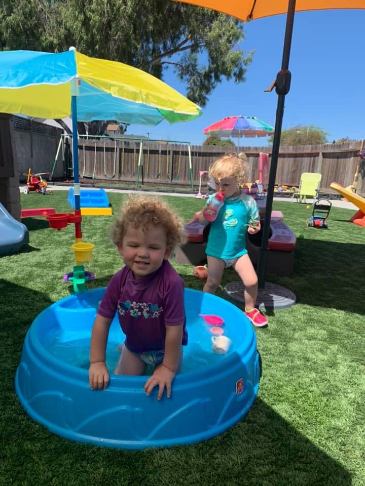 Two children playing outdoors, one in a small blue pool