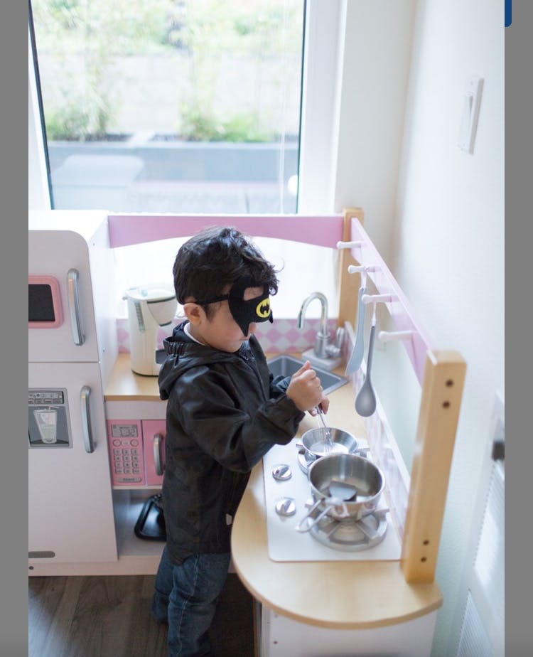 Child in a mask playing with a toy kitchen set
