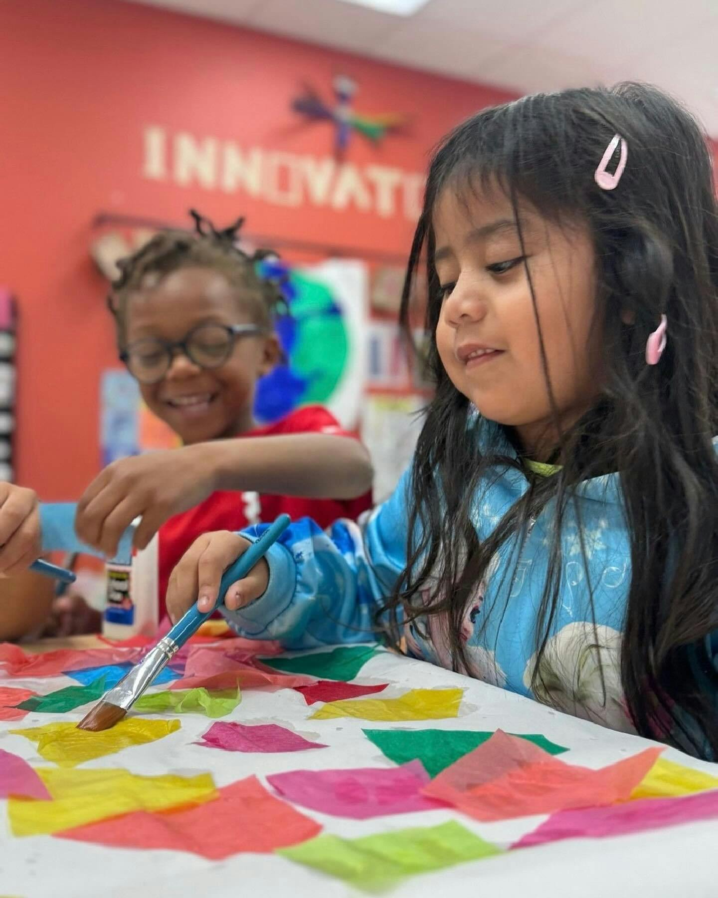 Two children doing an art project with colorful paper and paintbrushes