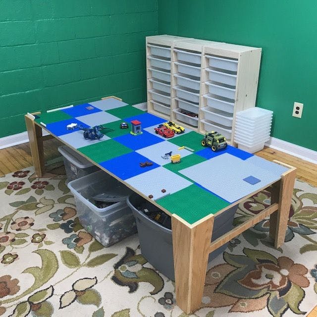 Table with blue, green, and gray building block baseplates and toy vehicles