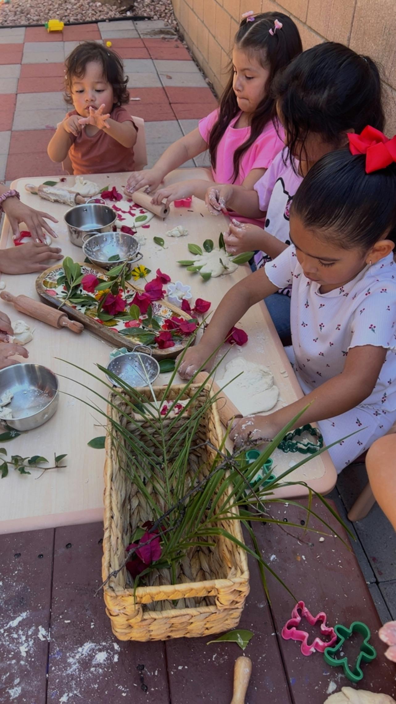 Group of children playing with dough and plant clippings at an outdoor table