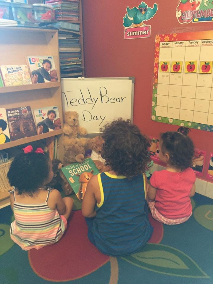 Children sitting on a rug reading a book with teddy bears and a whiteboard