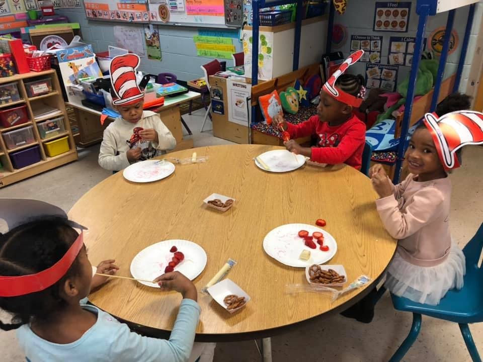 Children wearing striped hats sitting around a table with plates of plates of food