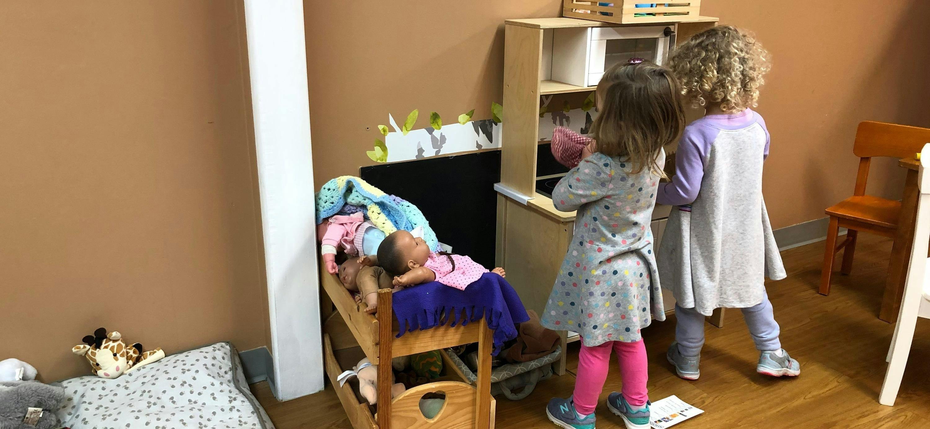 Two children playing with a doll and a toy kitchen