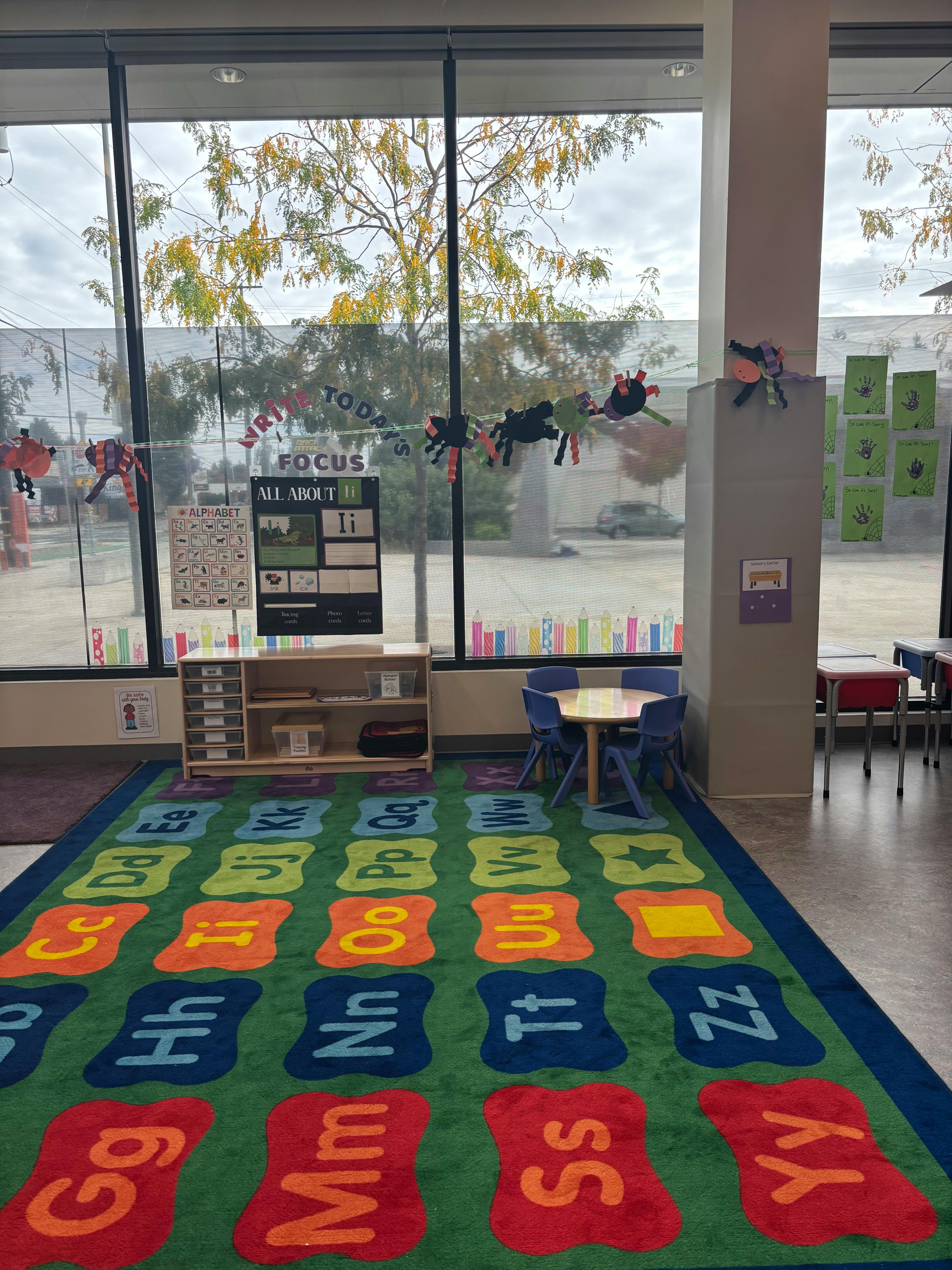 Classroom with alphabet rug, small table and chairs, and large windows