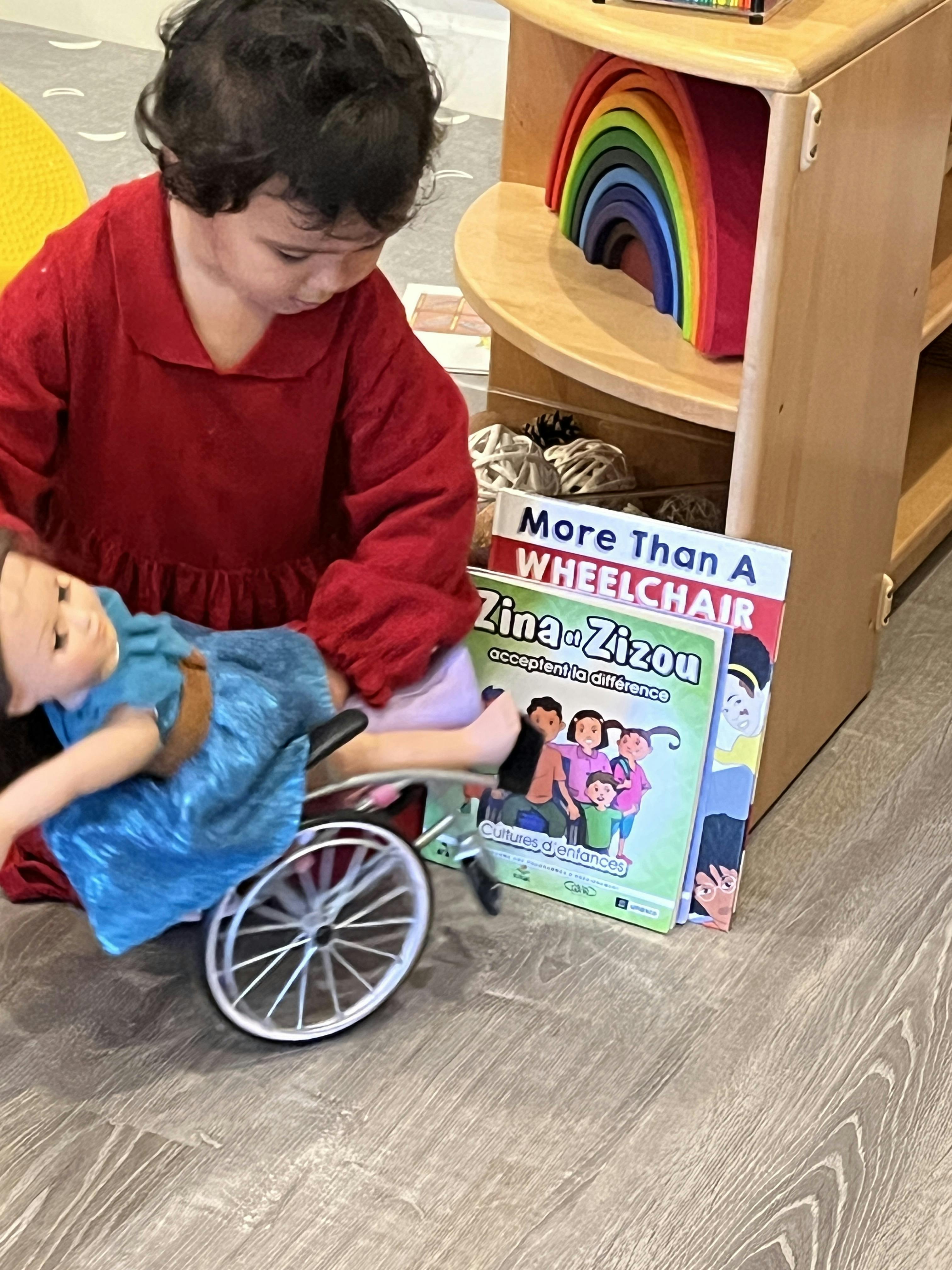 Child playing with a doll in a wheelchair near books about disabilities