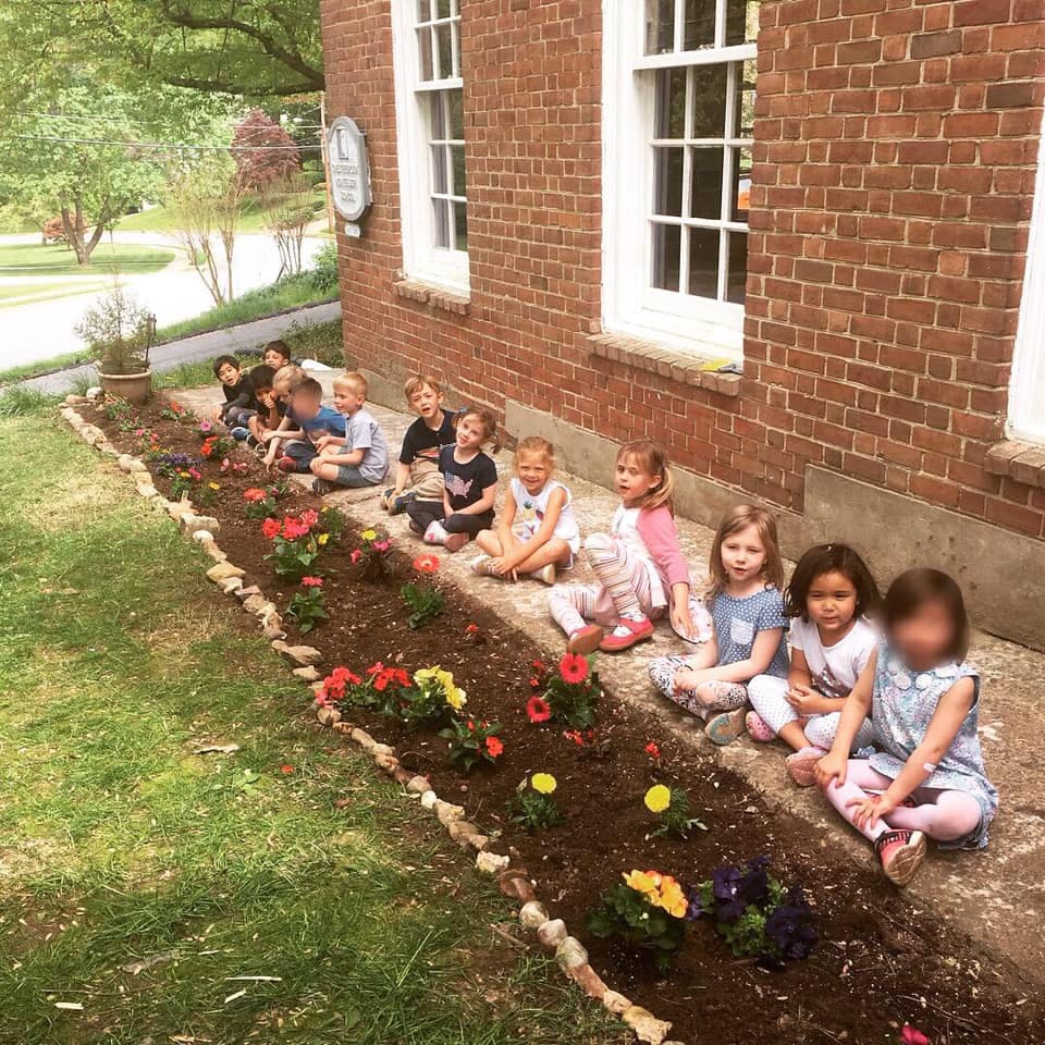 Children sitting by a flower bed next to a brick building