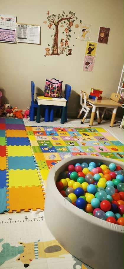 Playroom with colorful floor mats, small tables, chairs, and a ball pit