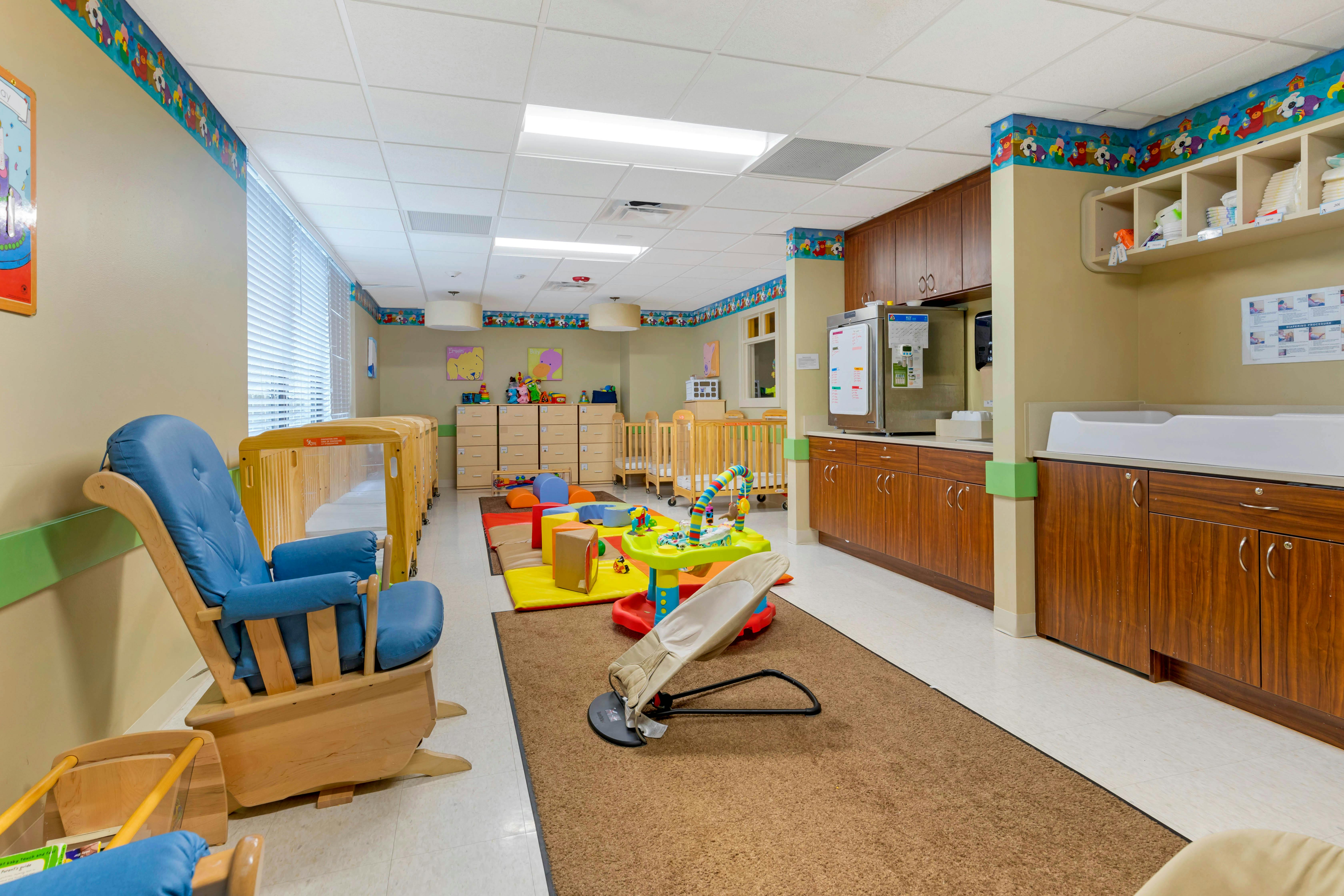 A colorful childcare room with cribs, play mats, and a changing station