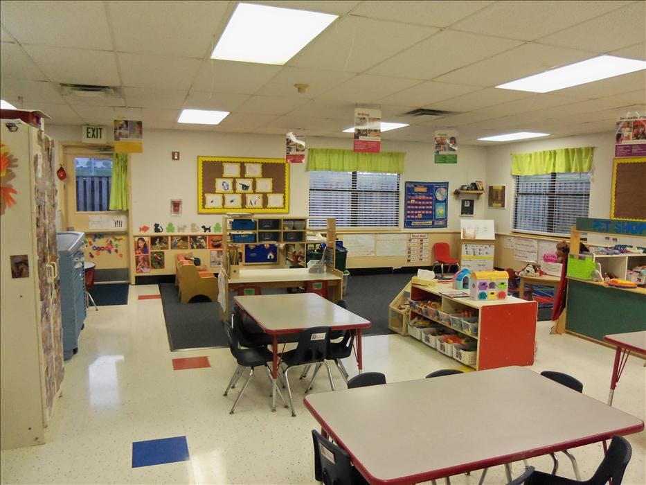 Empty classroom with small tables and chairs, toys, and educational posters