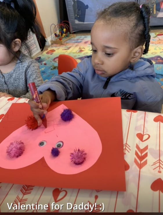 Child making a heart-shaped craft with pom-poms and googly eyes