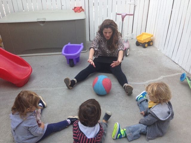 Person sitting on ground with three children and a ball