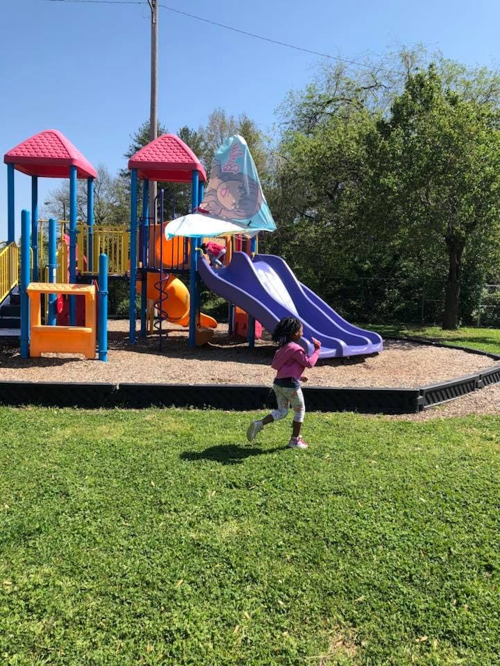 Child running on grass toward a playground with slides