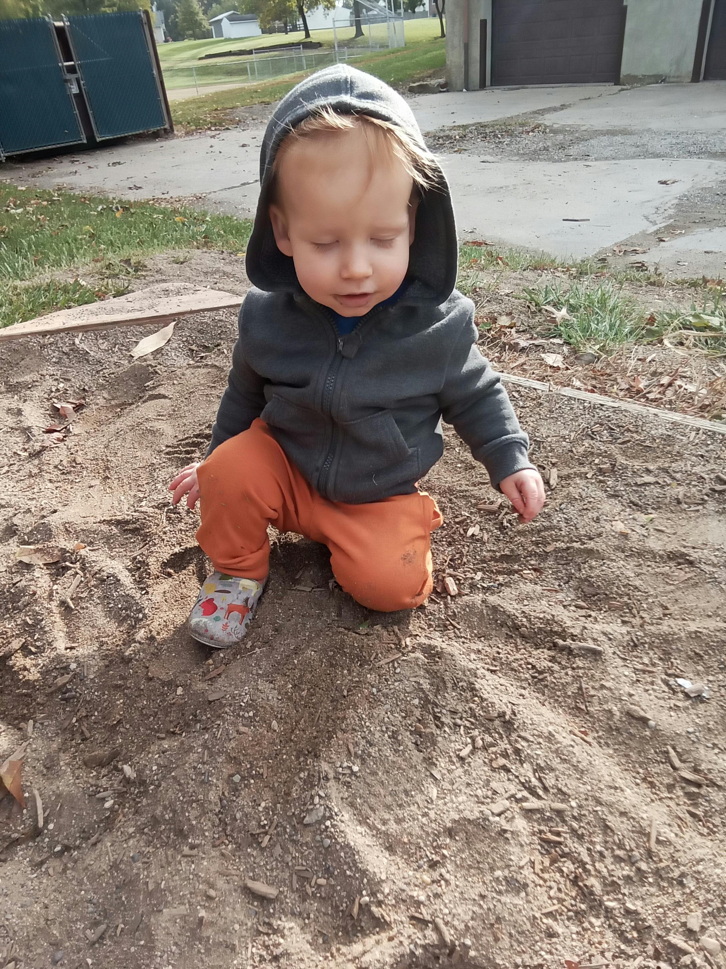 Child in a hooded jacket kneeling and playing in the dirt