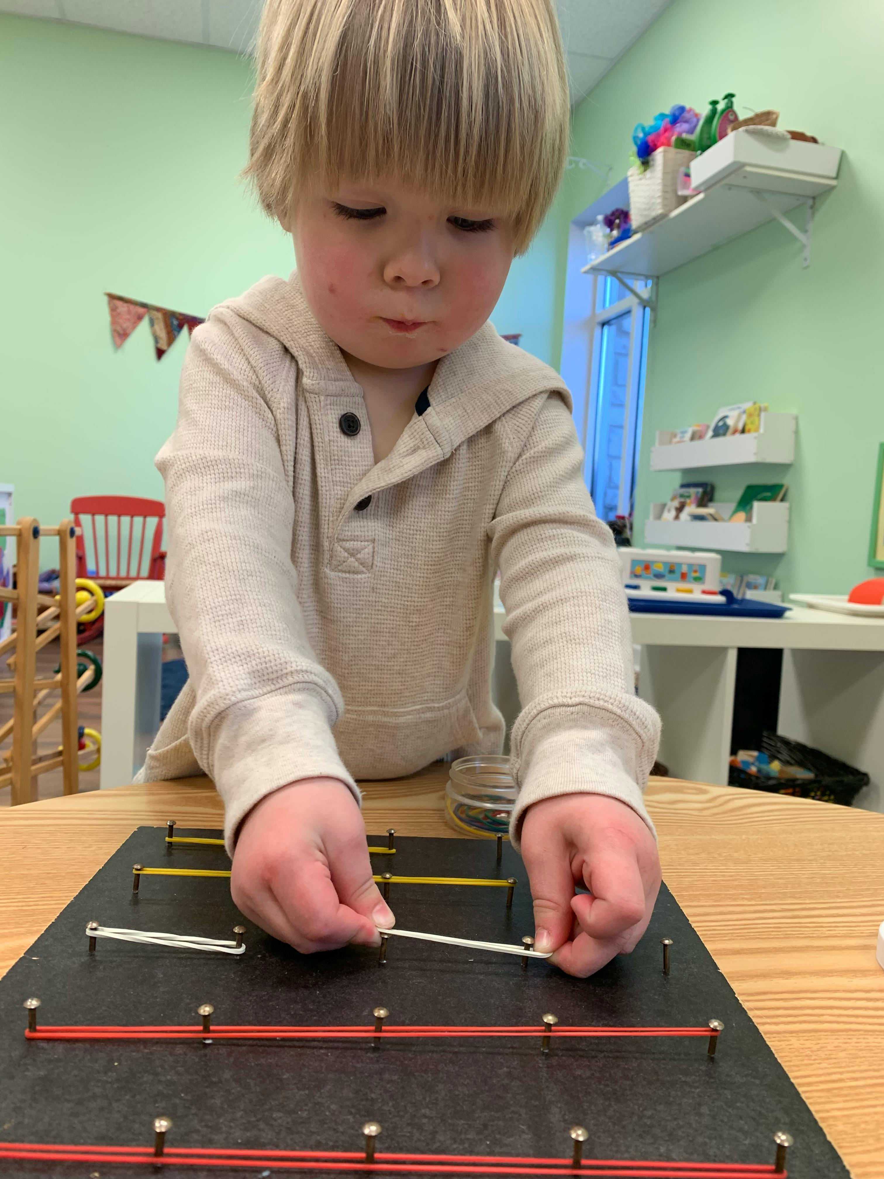 Child playing with a geoboard and rubber bands