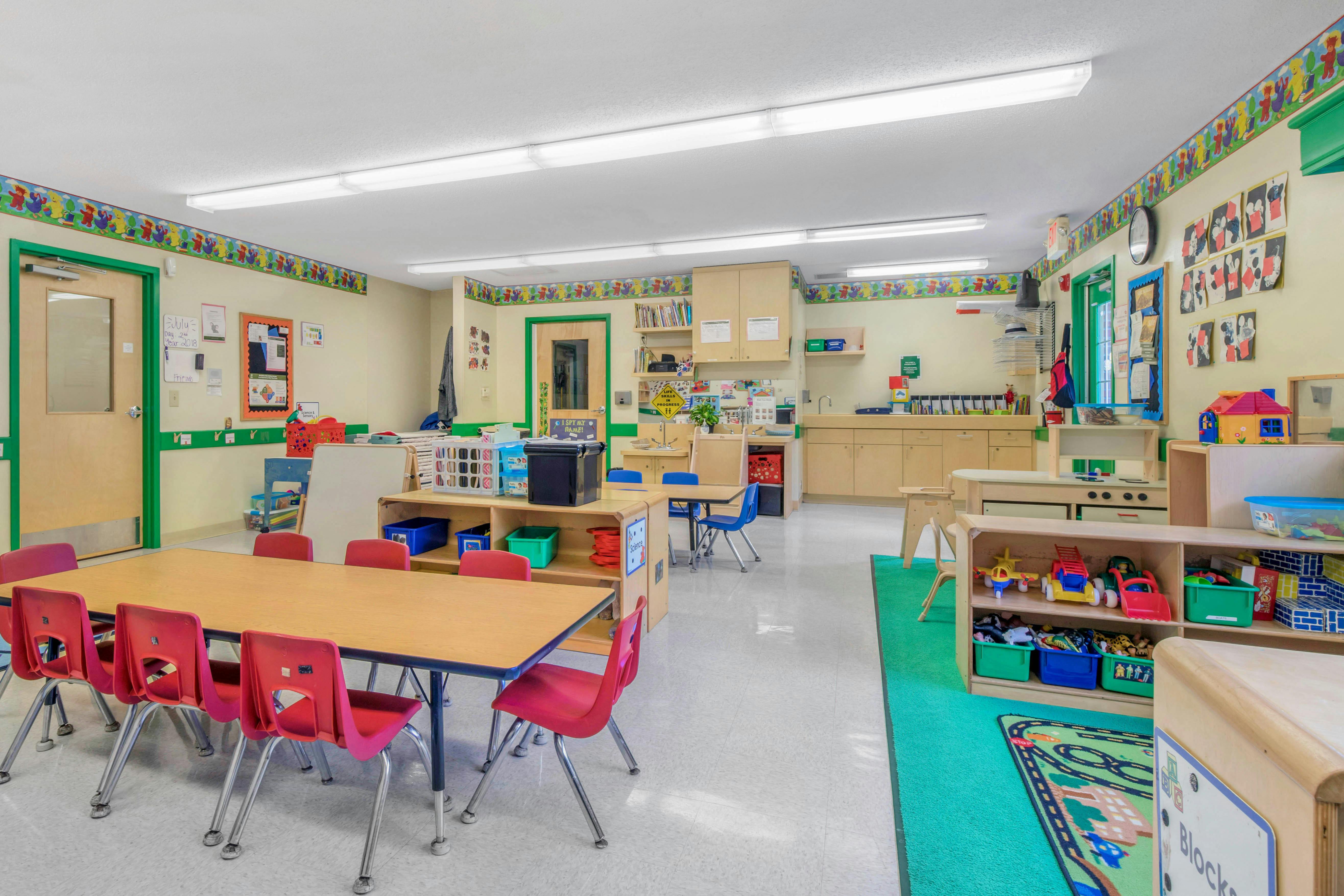 Classroom with tables, chairs, shelving with toys, and wall decorations