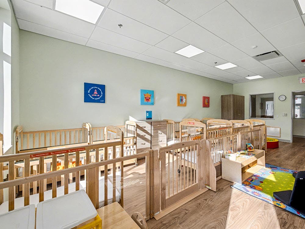multiple wooden cribs in a daycare room with a colorful rug and small furniture