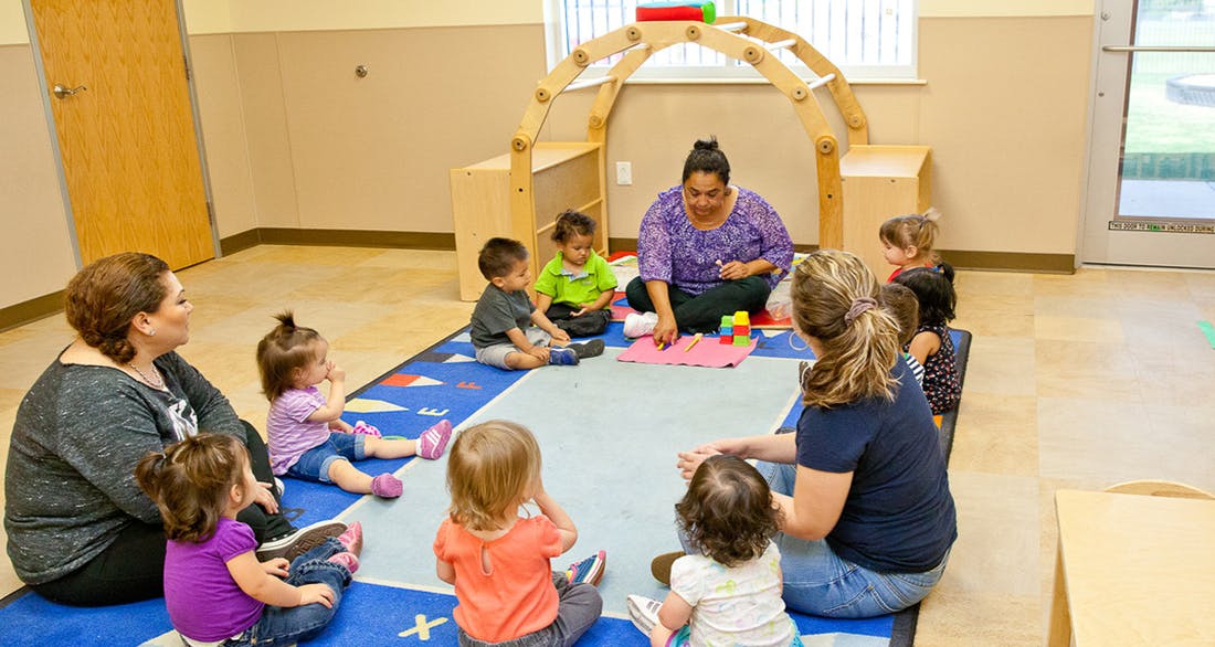 Adults and children sitting on a rug in a classroom