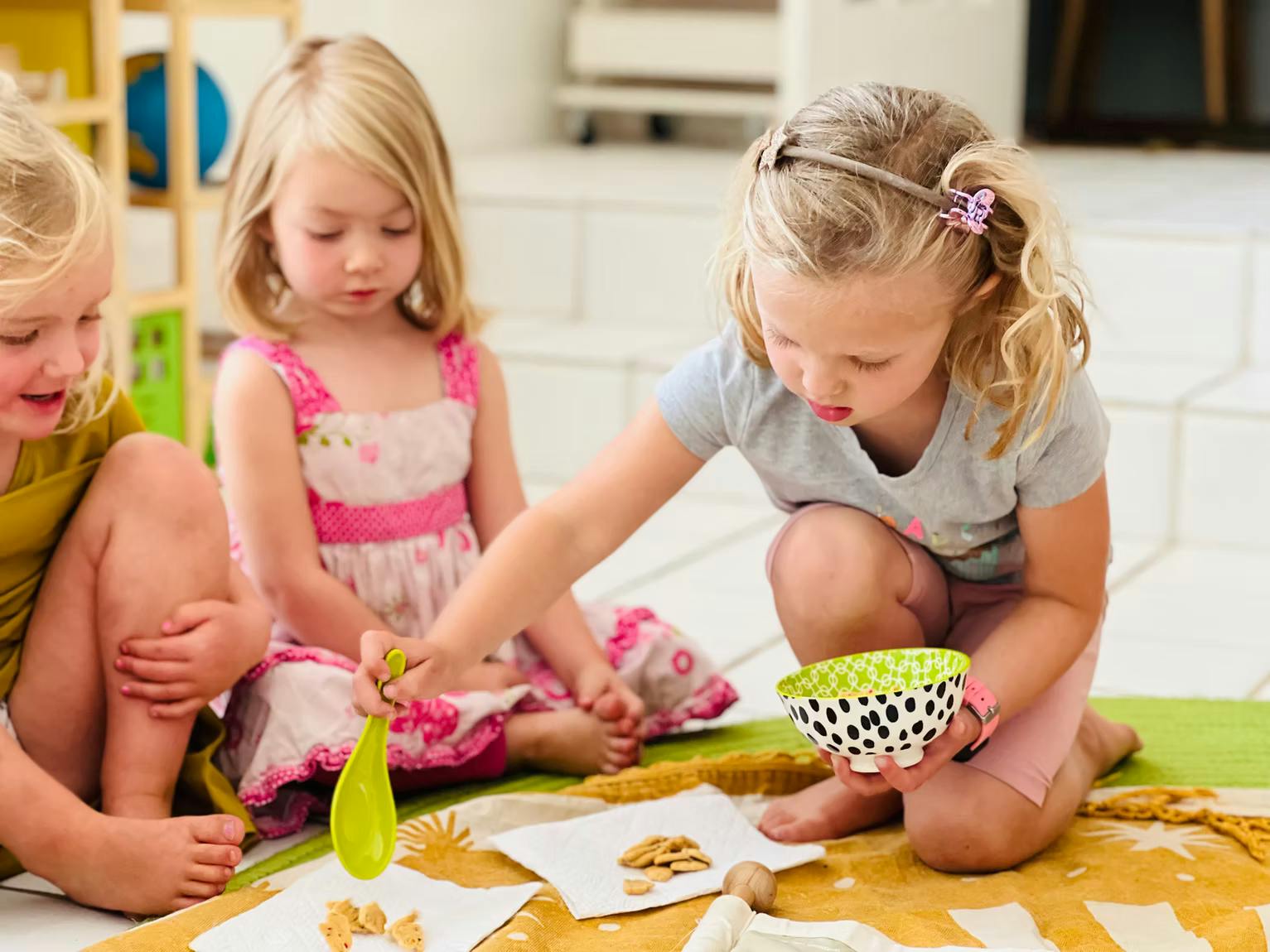 Three children playing with crackers and a bowl on the floor