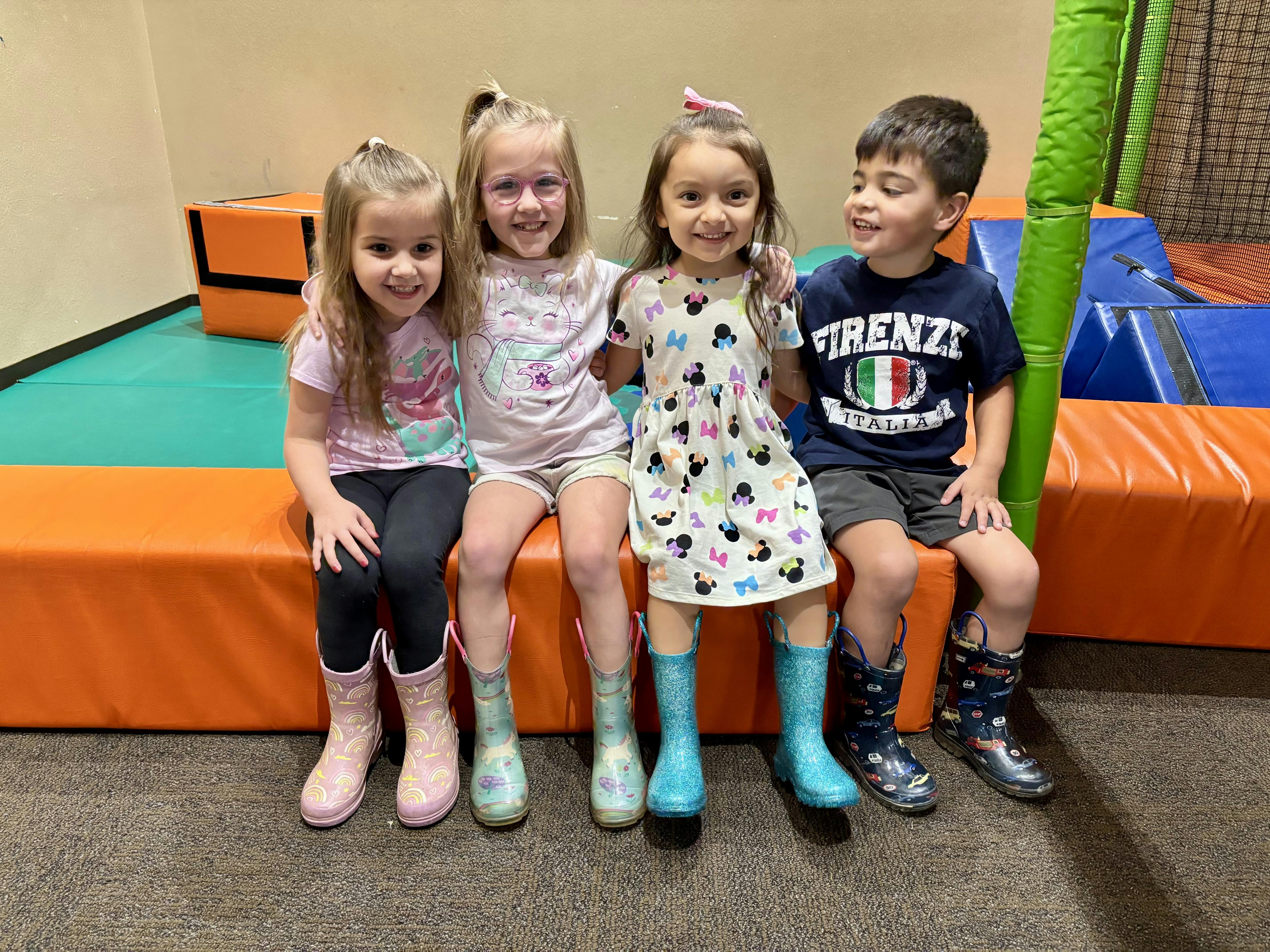 Four children sitting together on a soft play structure wearing rubber boots