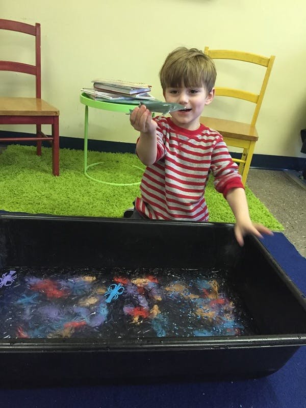 Child holding a toy over a bin of water with colorful objects