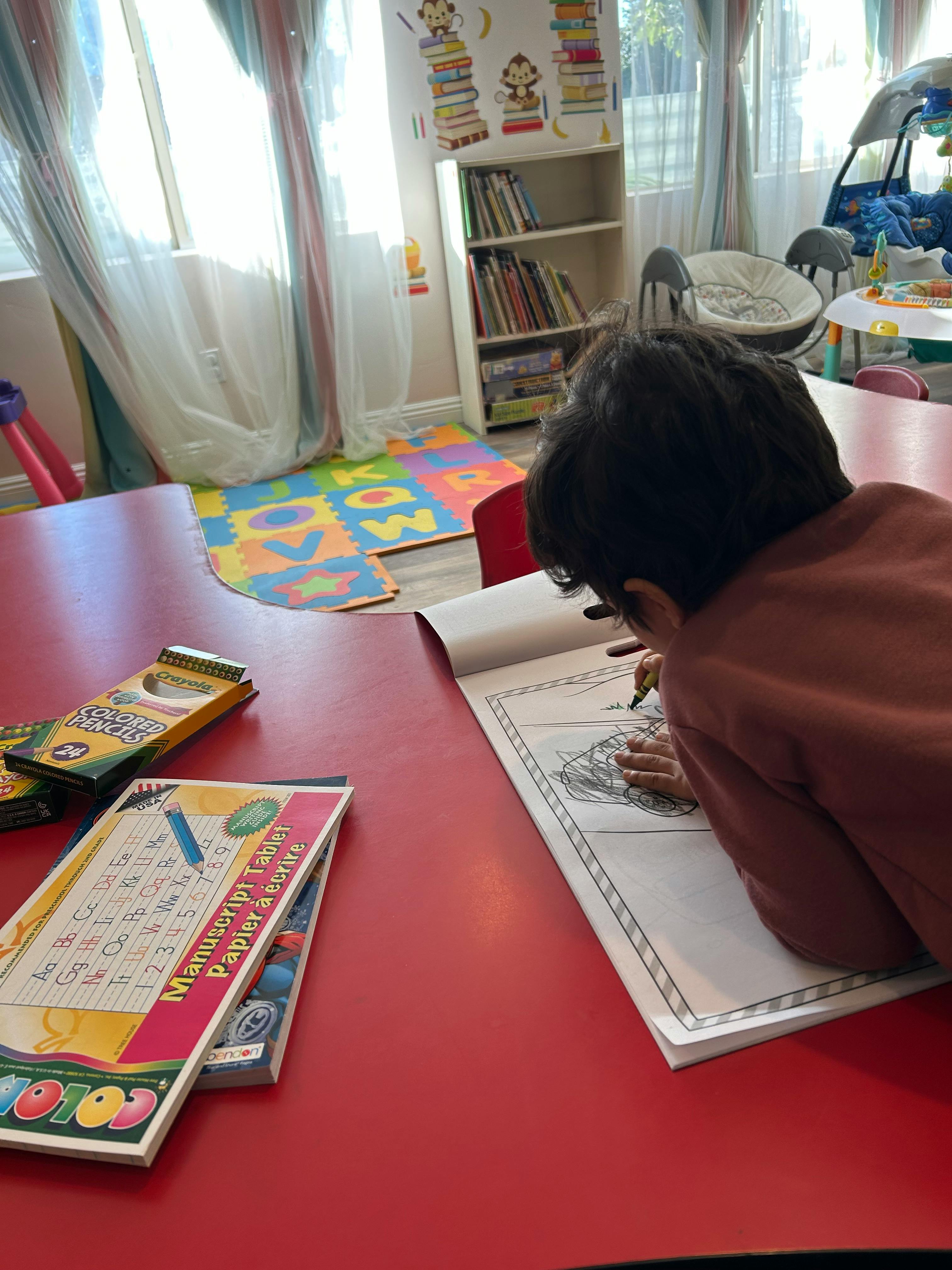 Child drawing in a book at a red table
