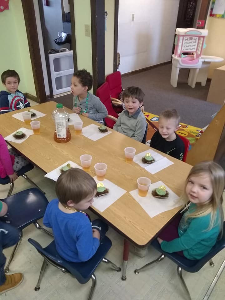 Children sitting at a table with drinks and small cakes