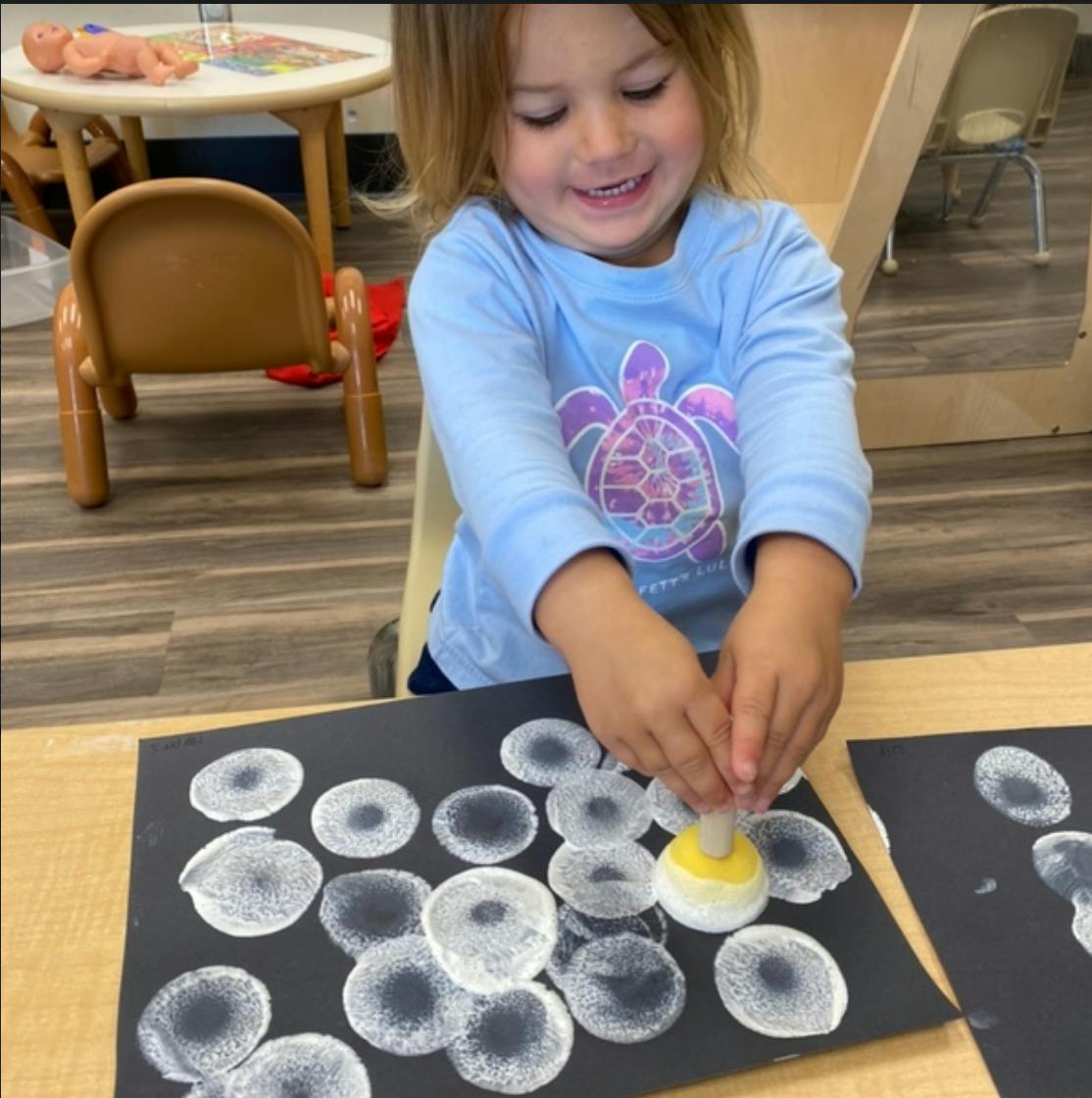 Child making white circle prints on black paper