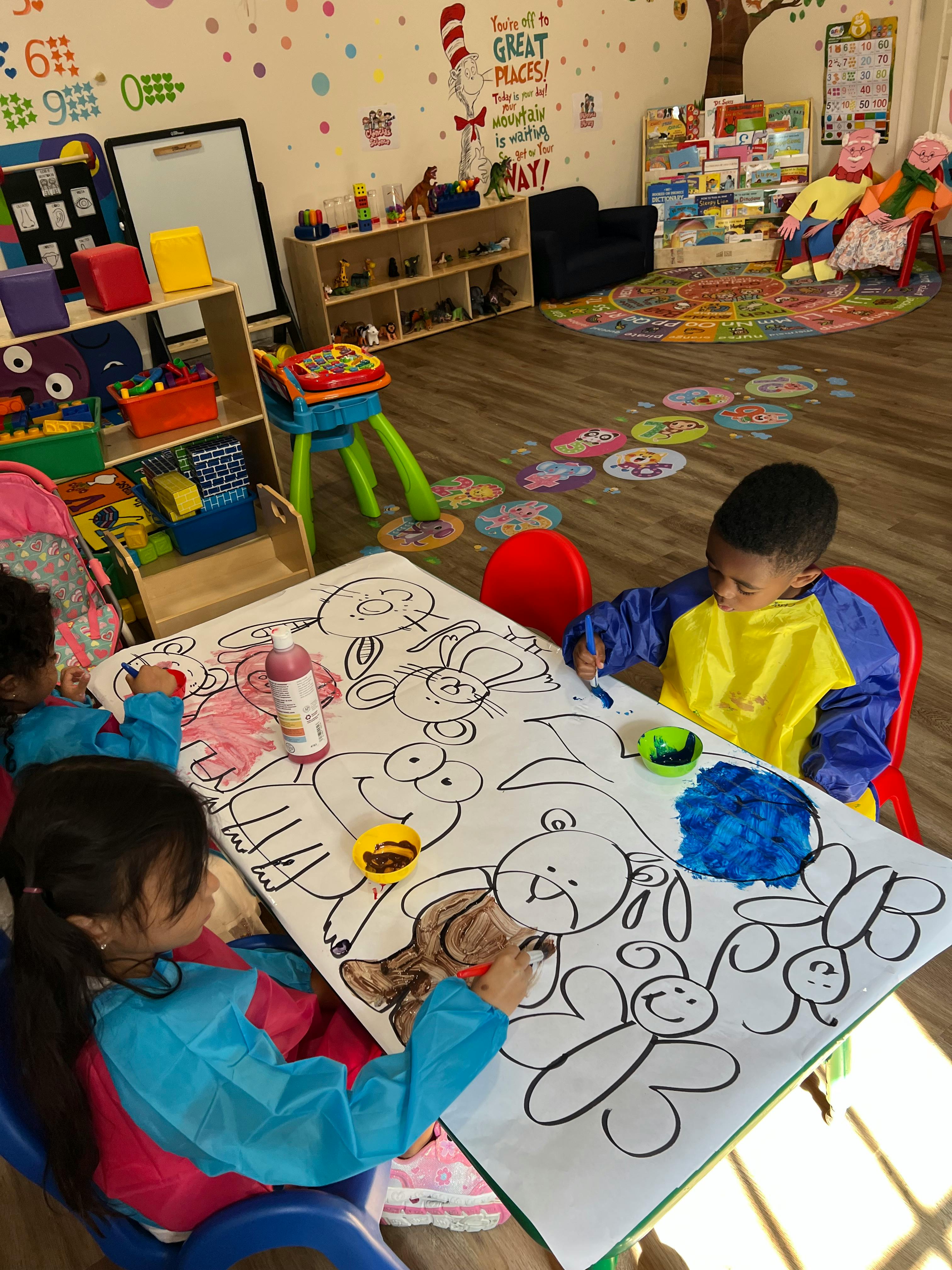 Two children painting on a large sheet of paper with cartoon outlines