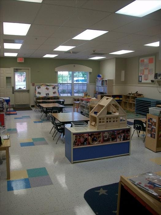 An empty classroom with small tables and chairs, a playhouse, and an exit sign