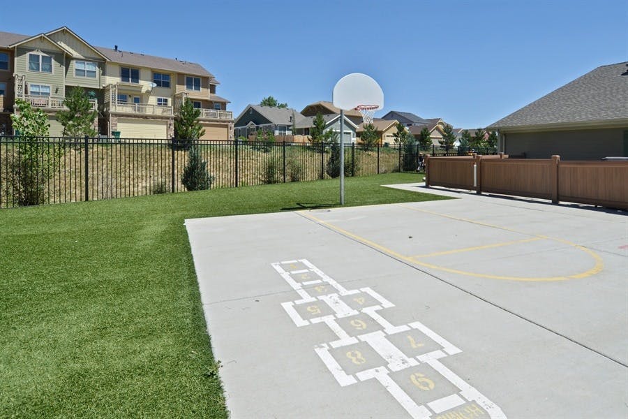 Outdoor court with hopscotch and basketball hoop next to grass and buildings