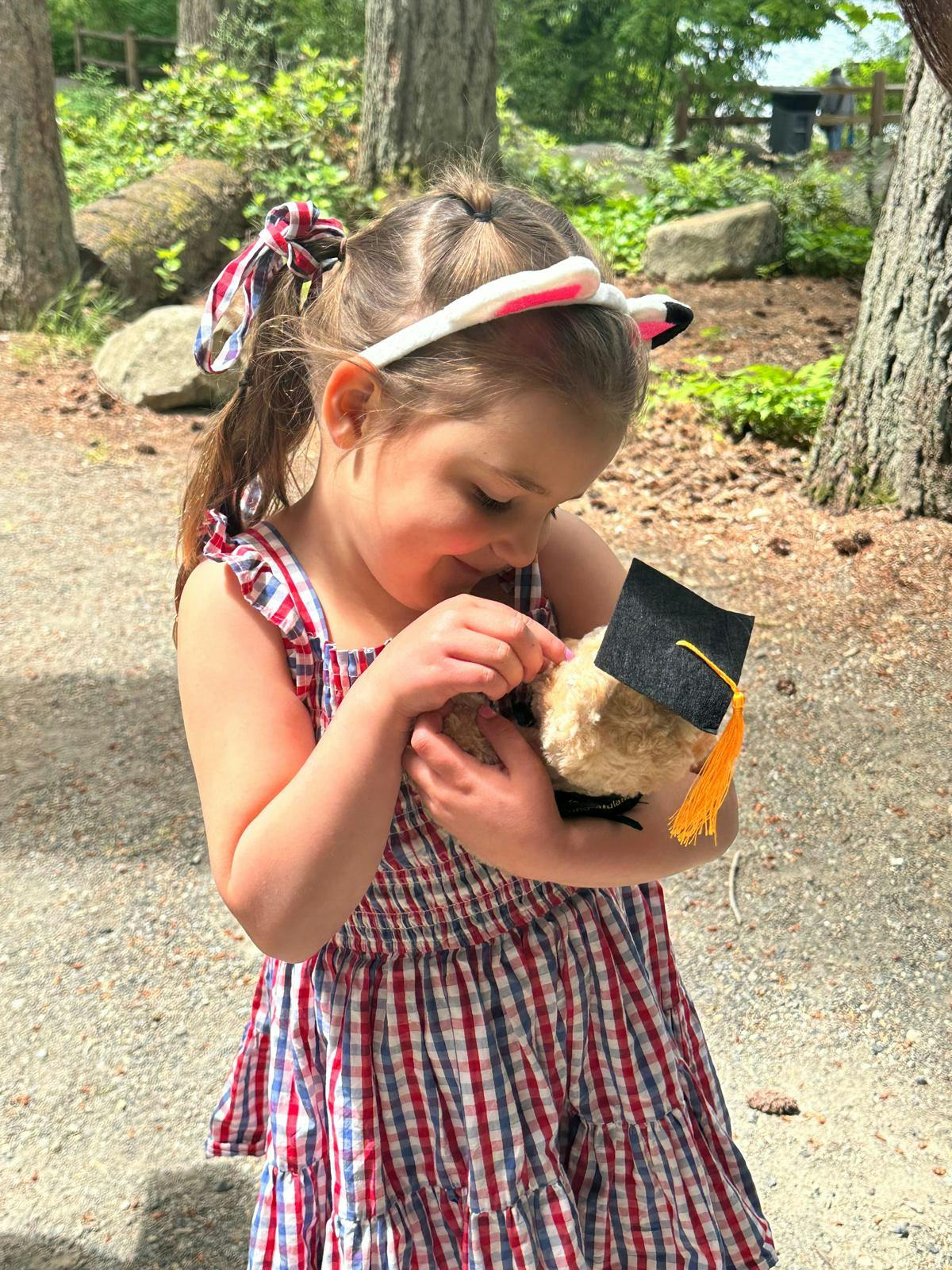 Child holding a small teddy bear wearing a graduation cap