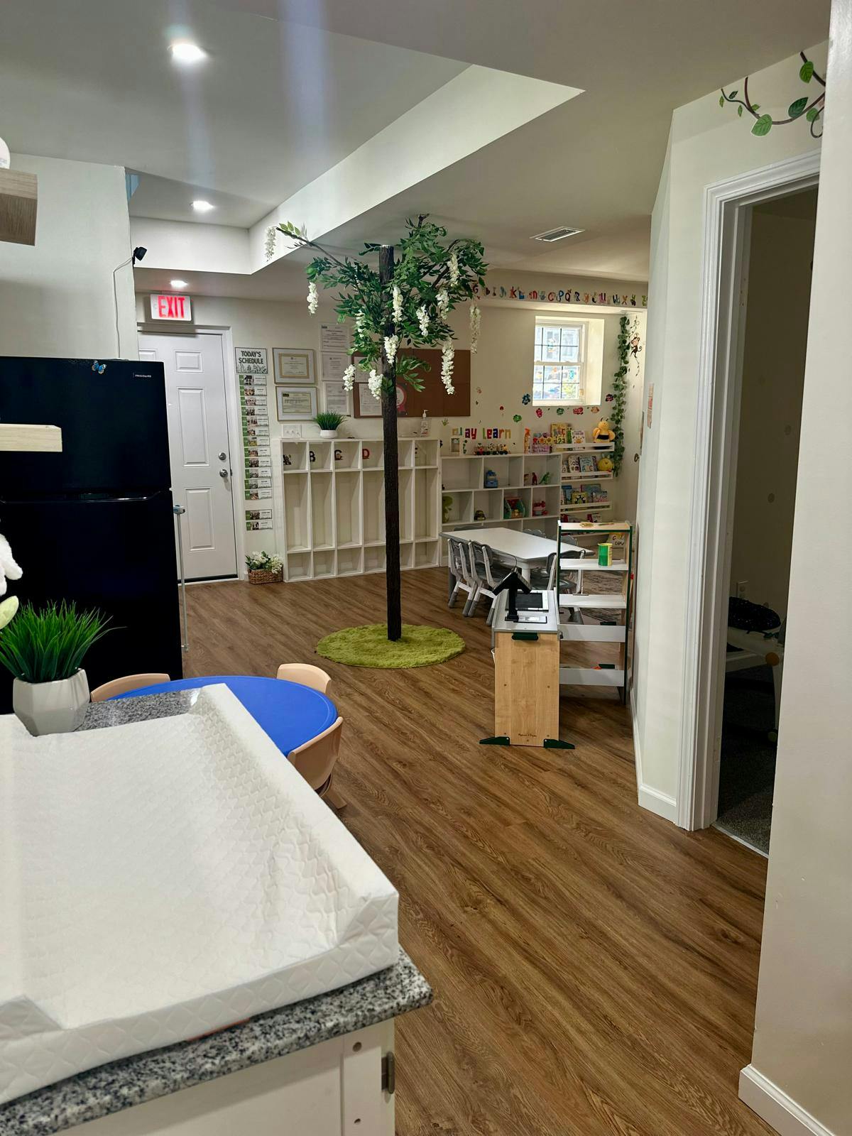 A childcare room with a play tree, small tables, shelves of toys, and a changing pad
