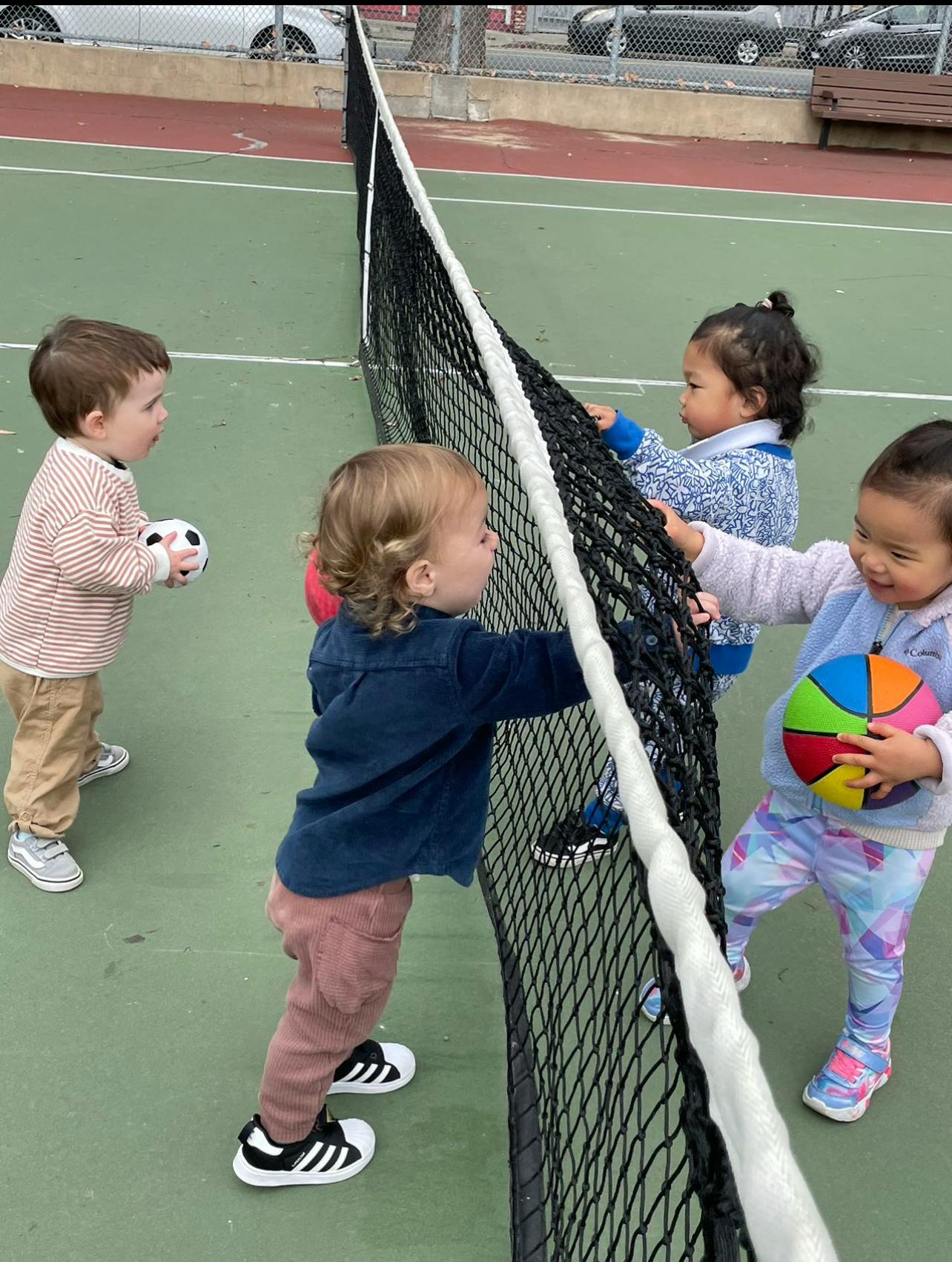 Four children playing with a net and balls on a tennis court