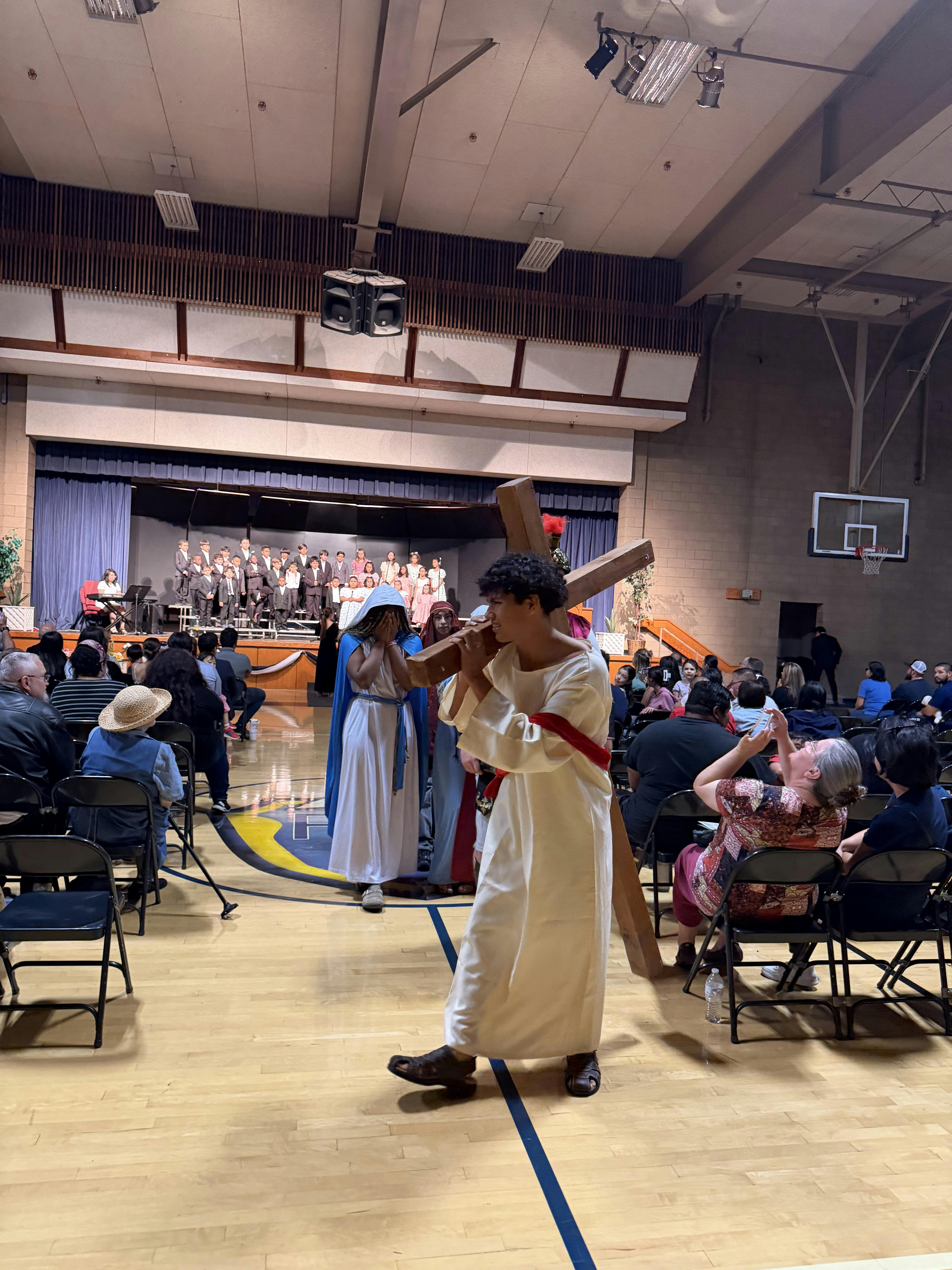 People in costumes walking with a wooden cross through a gymnasium