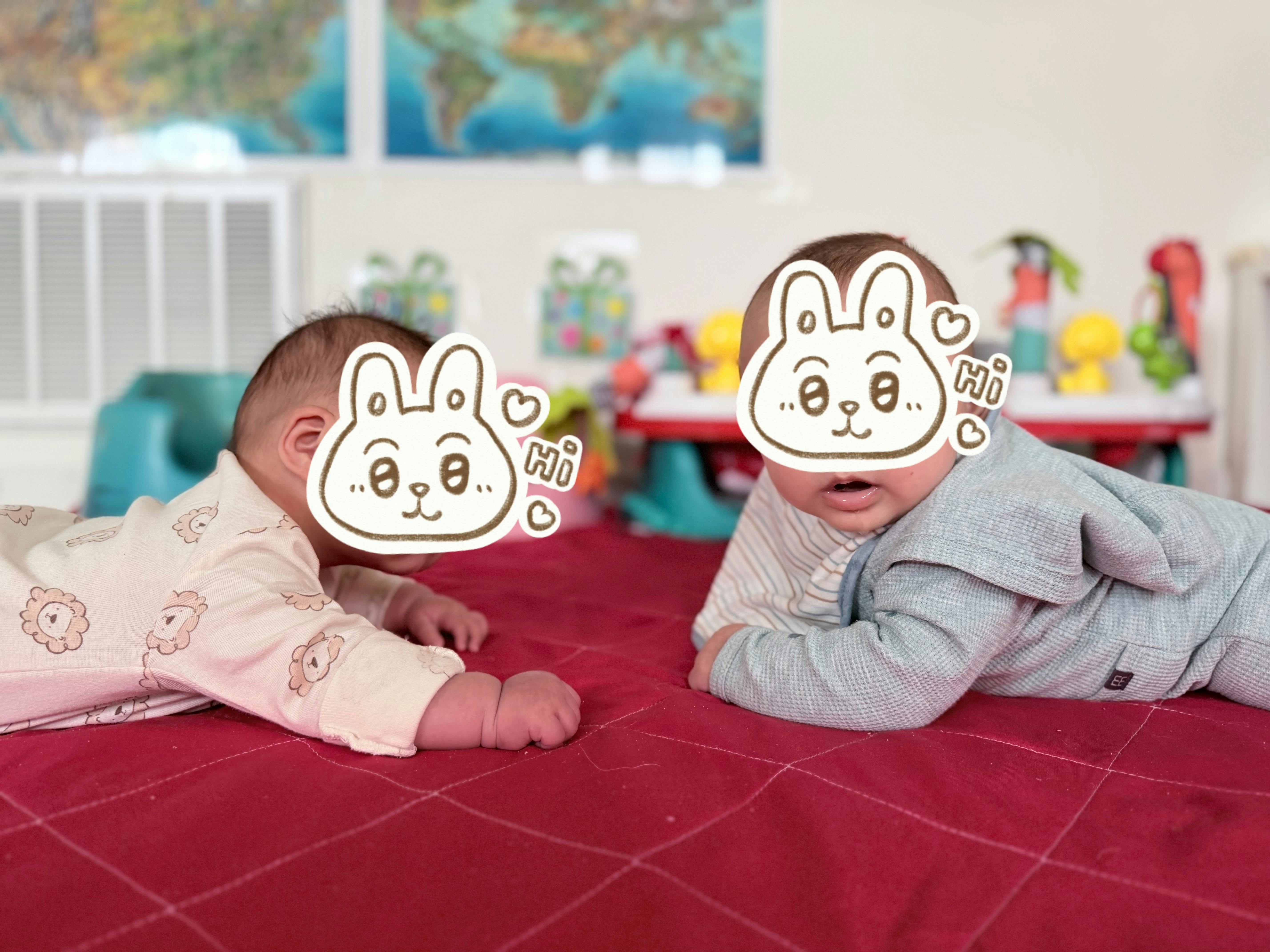 Two infants lying on their stomachs on a red blanket