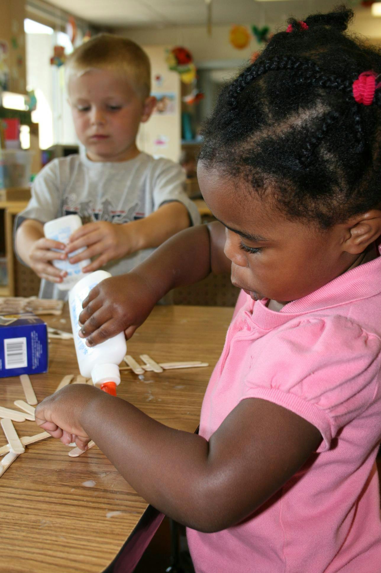 Two children gluing craft sticks in a classroom