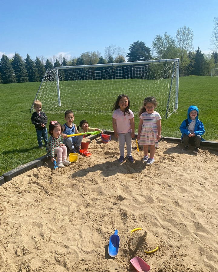 Children playing in a sandbox with a soccer goal in the background