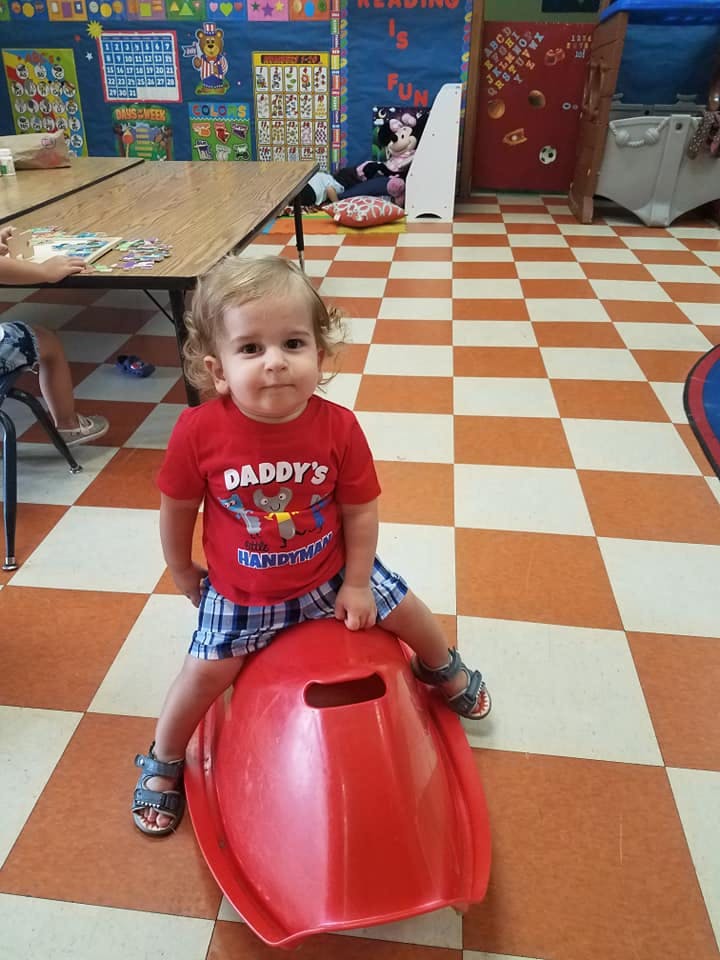 Child sitting on a red toy in a classroom