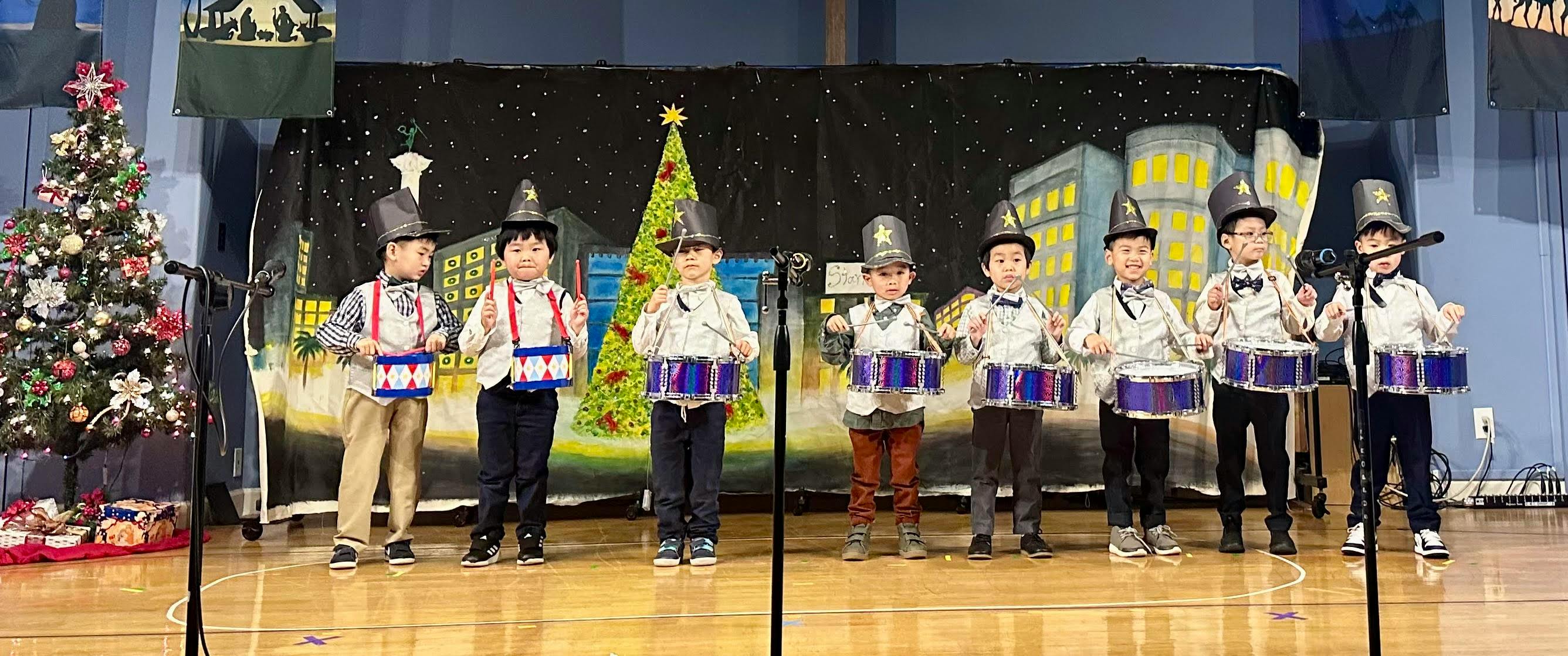 Group of children wearing hats and vests playing snare drums on a stage