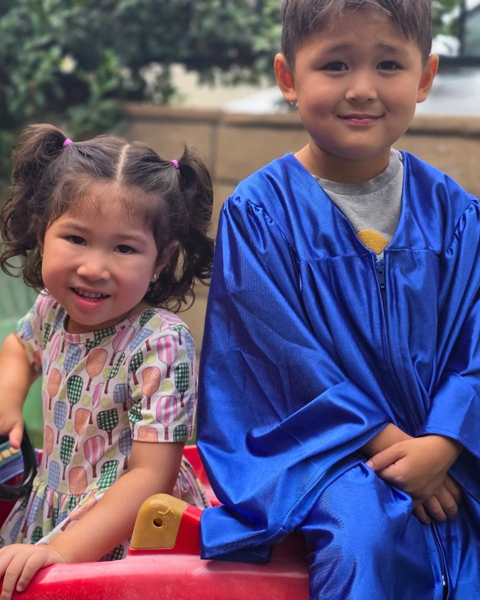 Child in blue graduation gown next to a child in a patterned dress